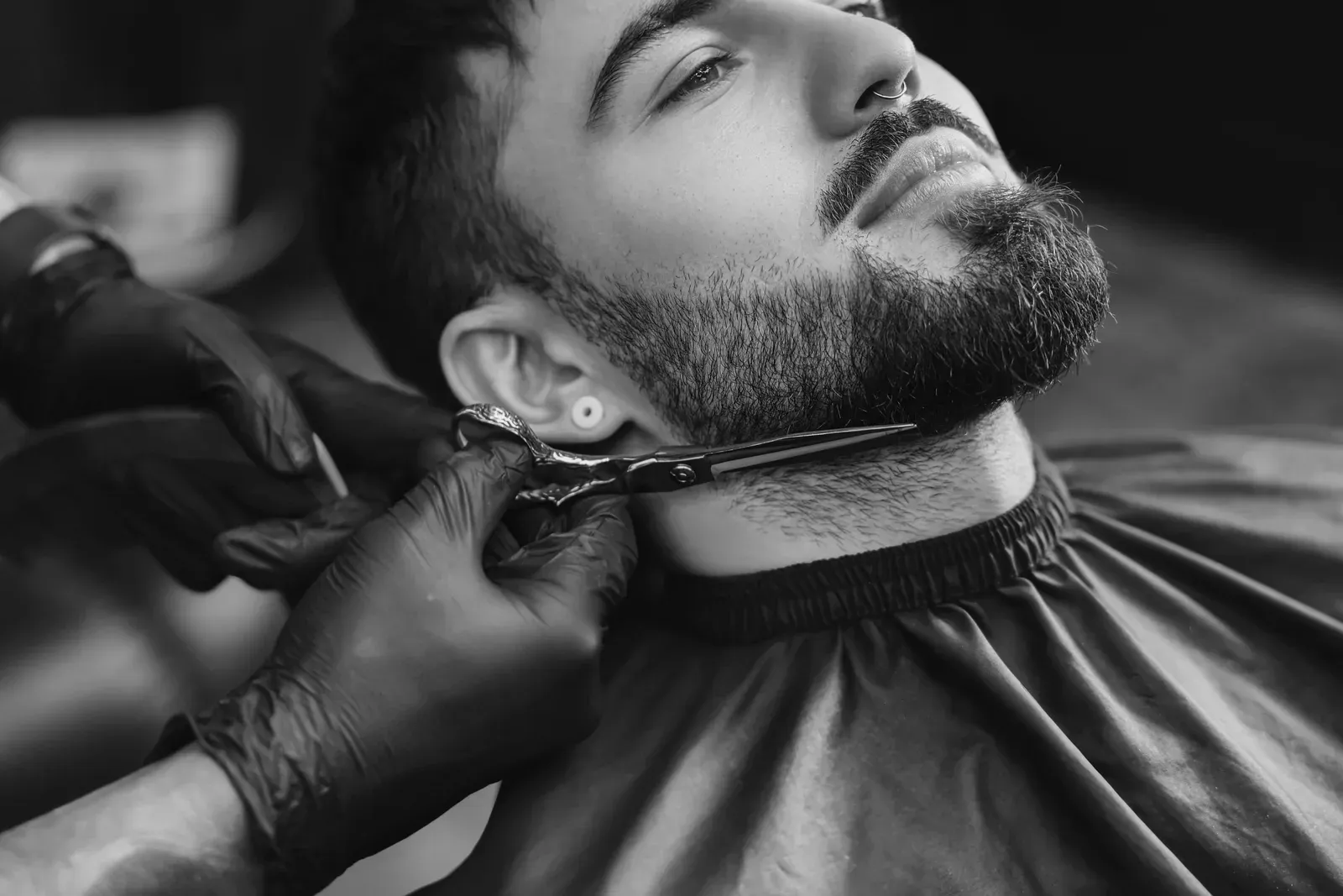Black and white photo of a barber lining up a client’s beard