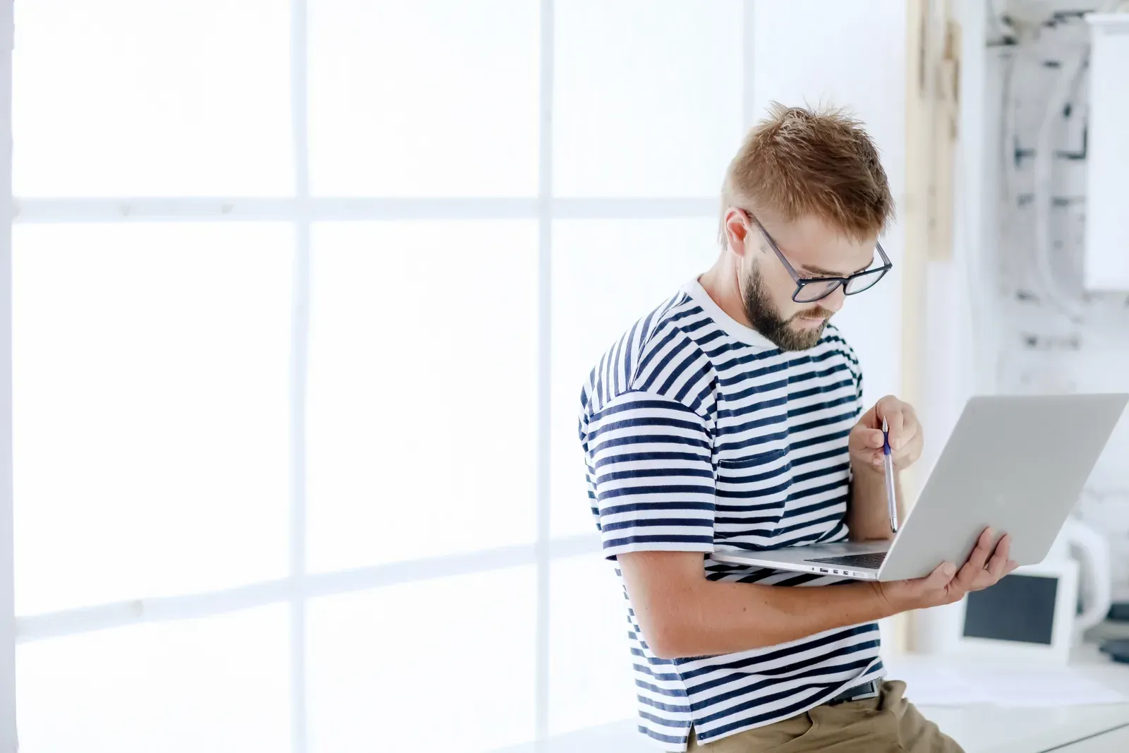 Man with glasses and a beard working on a laptop in an office