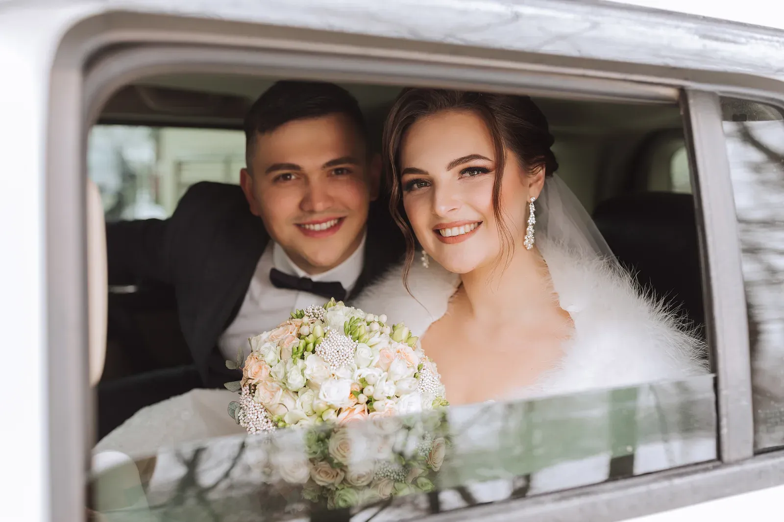 Smiling groom in a tuxedo and bride in a wedding car