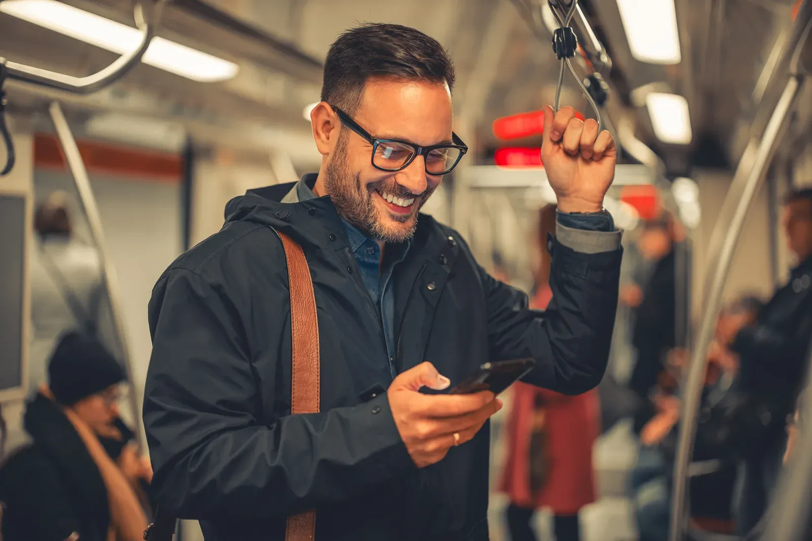 Man with glasses and a short beard smiling at his phone on a train