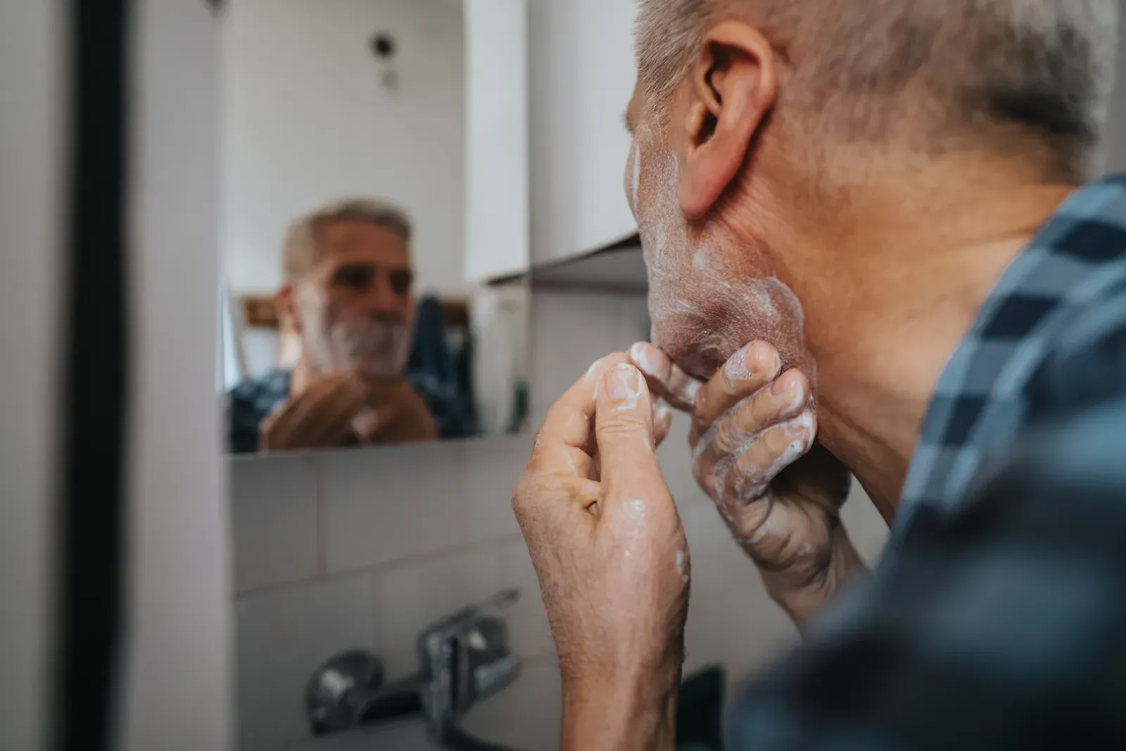 Older man checking his shave in a bathroom mirror