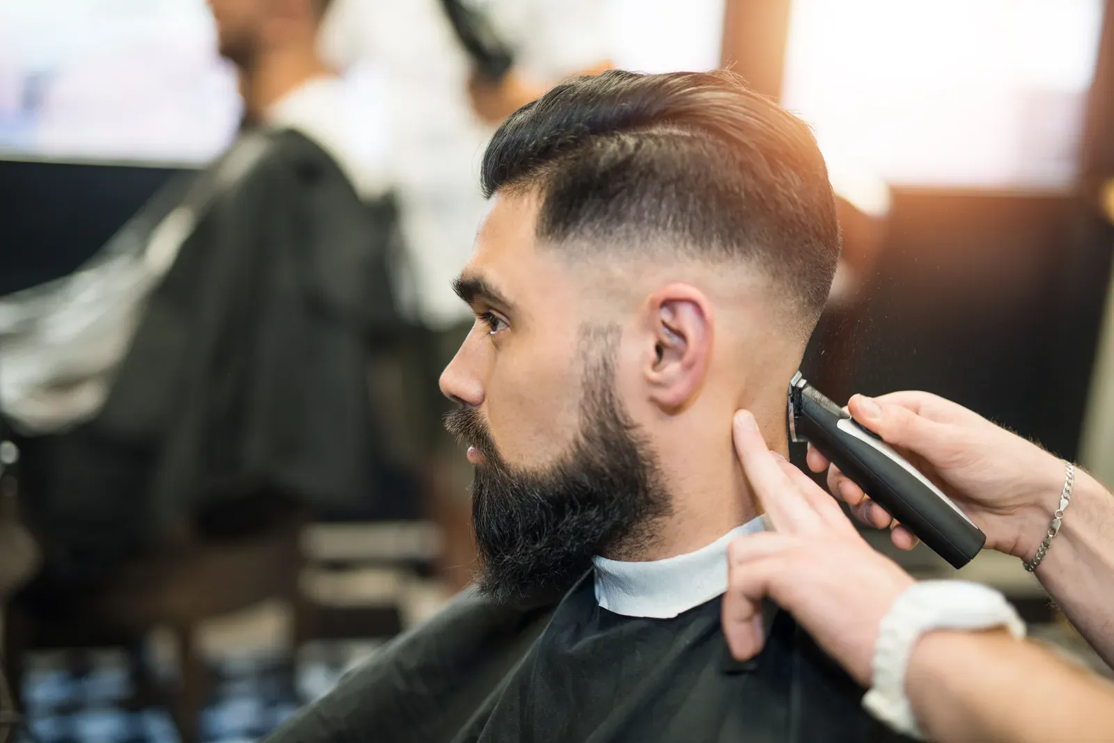 Barber blending a skin fade with clippers on a bearded client